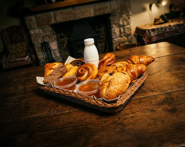 Édes péksütemények — croissant, kakaós csiga és briós — kosárban, lekvárokkal és tejjel
